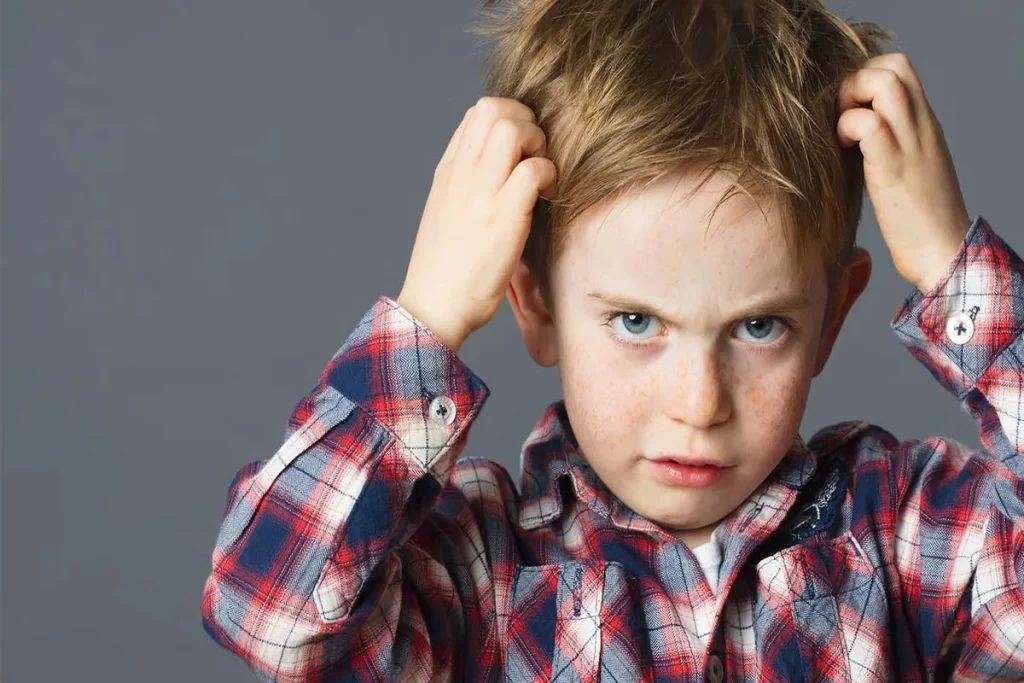 Criança coçando a cabeça com expressão de incômodo, sinal comum de infestação por piolho.