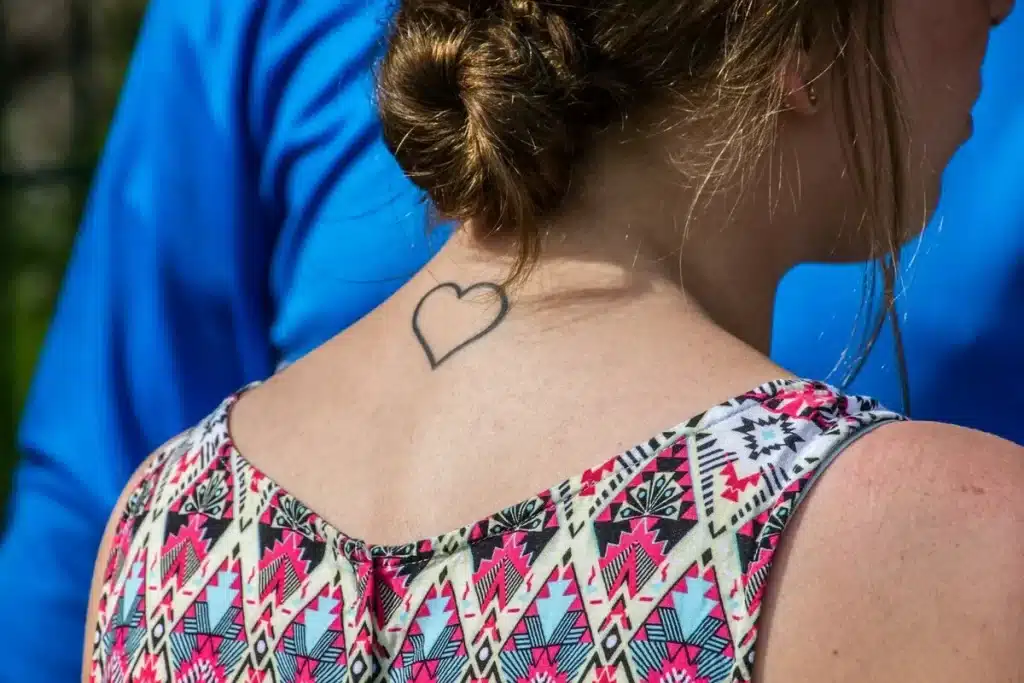 Tatuagem de coração simples na nuca de uma mulher, representando o amor pelos filhos.