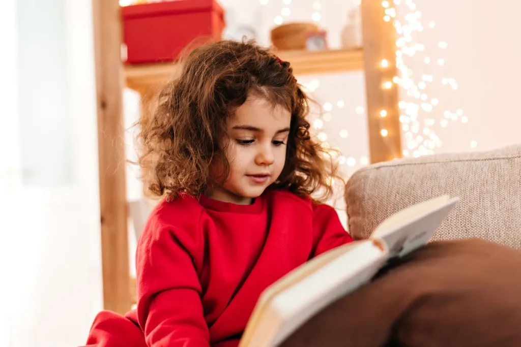Menina pequena lendo livro sentada no sofá com luzes decorativas ao fundo
