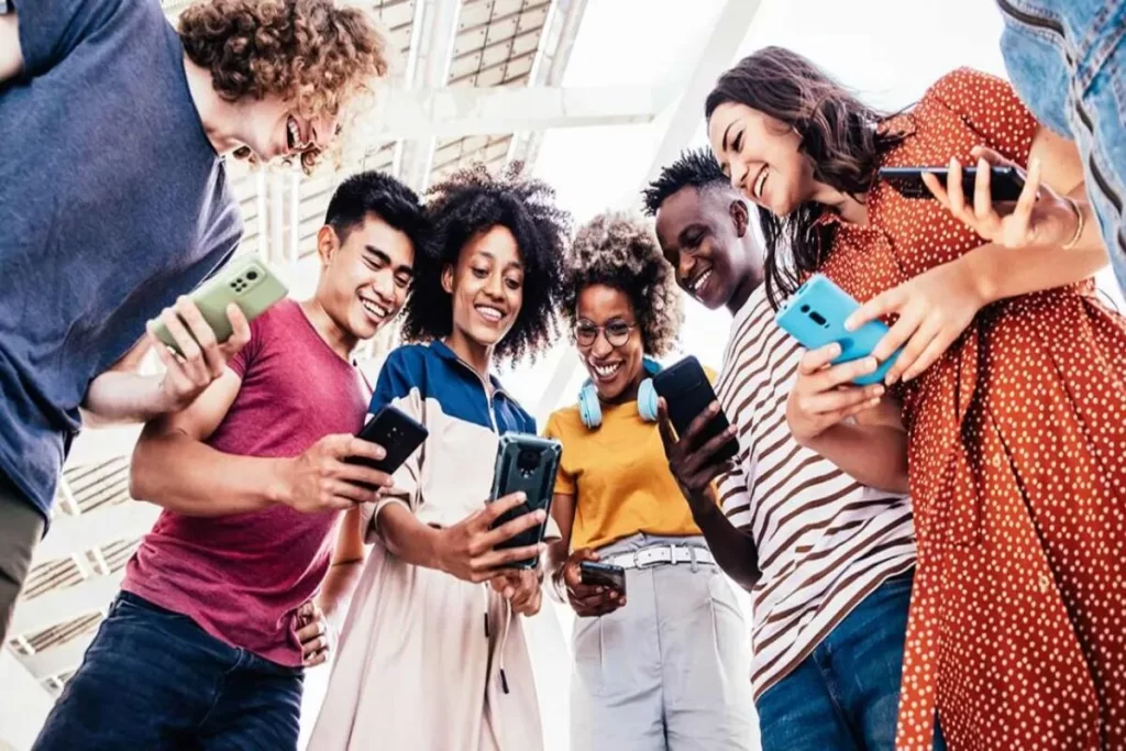 Grupo de jovens da Geração Z reunidos, sorrindo e interagindo com smartphones, representando conectividade e uso intenso de tecnologia.