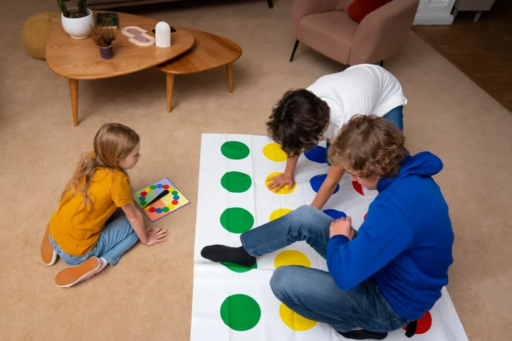 Crianças brincando em jogo educativo de coordenação motora com círculos coloridos dentro de casa, acompanhadas por um adulto.