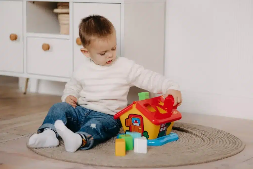 Criança brincando com brinquedo educativo de encaixe em formato de casinha colorida.