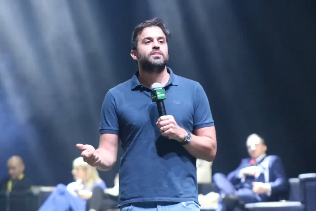 O empresário e coach Pablo Marçal em um palco escuro, segurando um microfone e gesticulando, durante uma palestra ou evento.