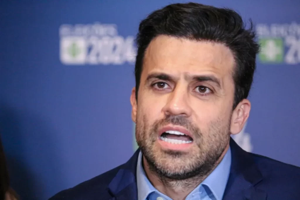 O empresário e coach Pablo Marçal, com uma expressão séria, em um estúdio com fundo de campanha política.