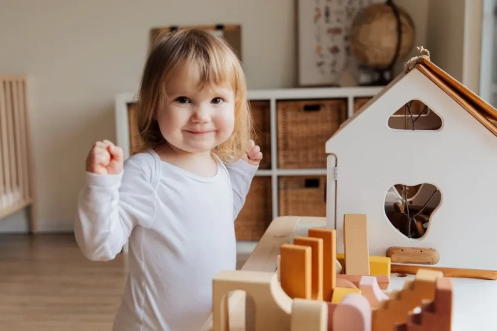 Menina sorridente de um ano brincando com blocos de madeira educativos em um ambiente infantil acolhedor.