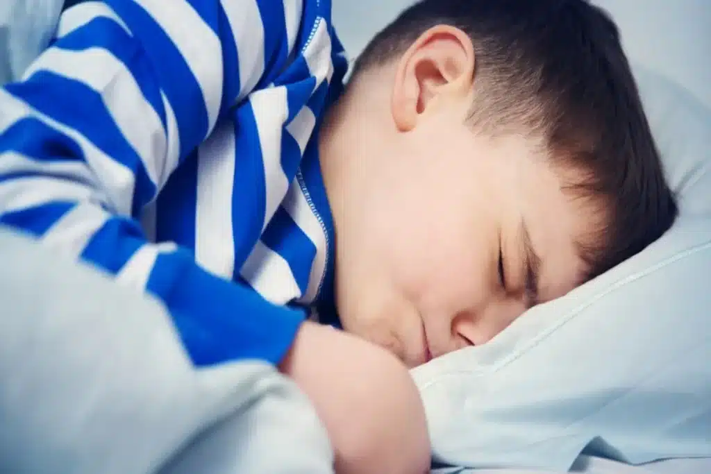 Menino dormindo com expressão de incômodo e rosto contra o travesseiro.