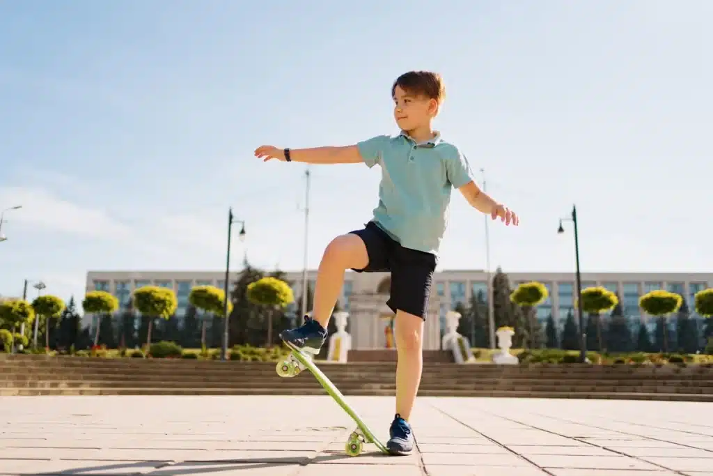 Menino praticando manobras com skate em uma praça ao ar livre em um dia ensolarado.