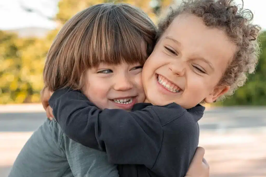 Dois meninos sorridentes se abraçando, demonstrando afeto e felicidade em um ambiente ao ar livre