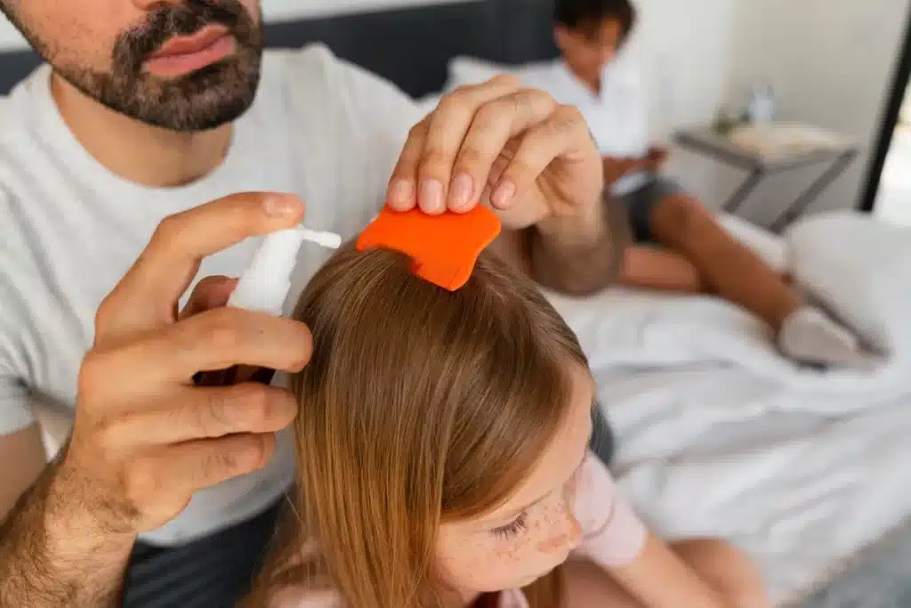 Pai usando pente fino e spray para tratar os cabelos da filha e remover piolhos em um ambiente doméstico