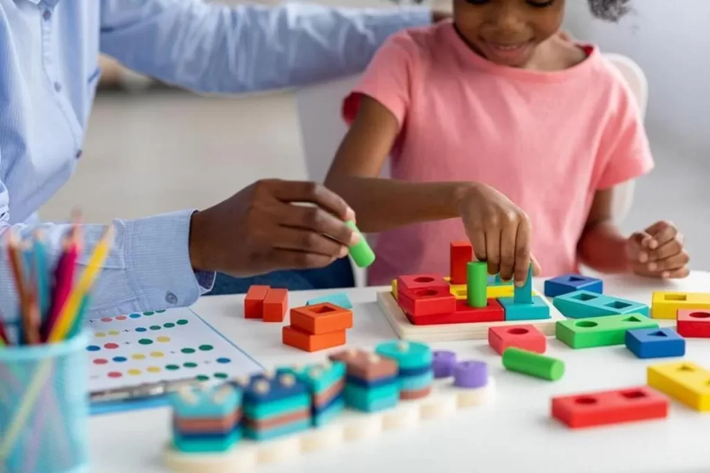 Criança se divertindo com brinquedo sensorial educativo colorido, encaixando peças de diferentes formas e cores em uma base de madeira.