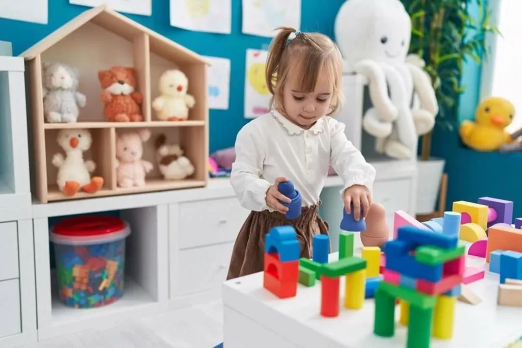 Menina brincando com brinquedo sensorial de blocos coloridos e formas geométricas em uma mesa educativa.