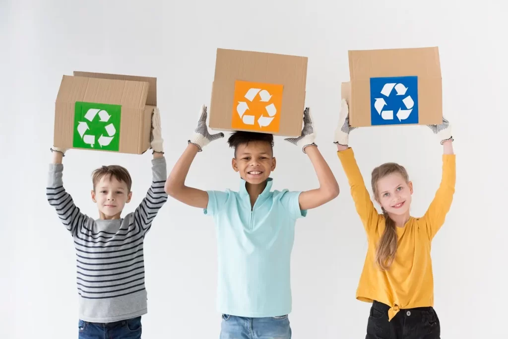 Três crianças com luvas segurando caixas de papelão com símbolos de reciclagem coloridos, sorrindo e promovendo a conscientização sobre o meio ambiente e a importância da reciclagem.