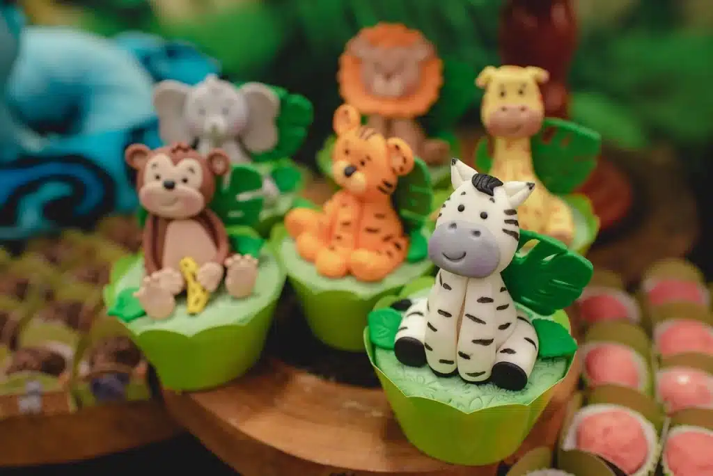 Doces decorados com animais da selva em festa infantil temática de safári para criança de 1 ano, com cupcakes personalizados de zebra, leão, girafa, elefante, tigre e macaco