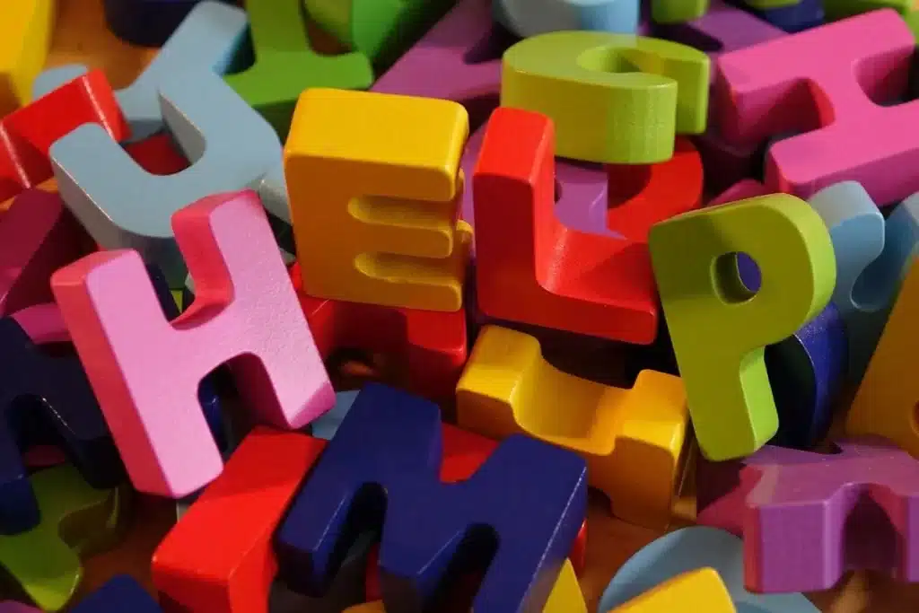 Letras do alfabeto coloridas em madeira espalhadas, com destaque para a palavra “HELP”. Material lúdico usado em atividades de alfabetização infantil.