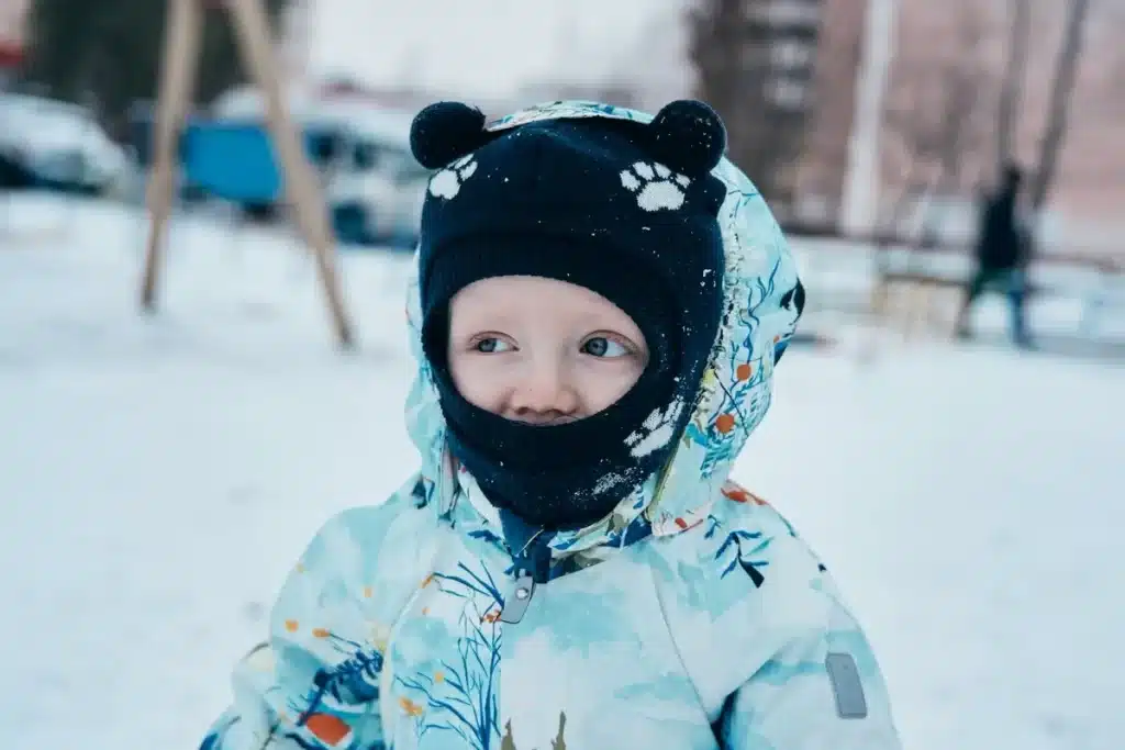 Criança com roupas de inverno brincando na neve em dia frio.