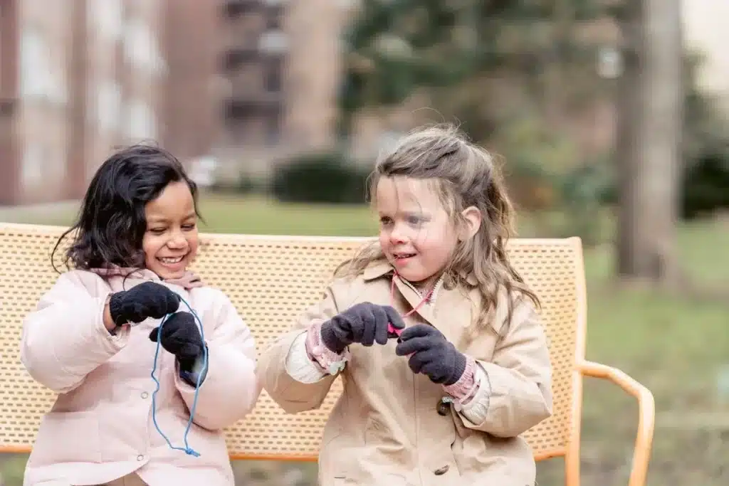 Crianças sorrindo e usando roupas de inverno em um banco ao ar livre.