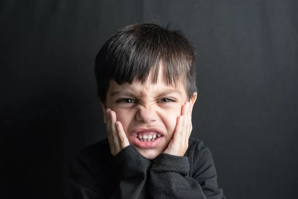 Criança com expressão de raiva, apertando o rosto com as mãos.  