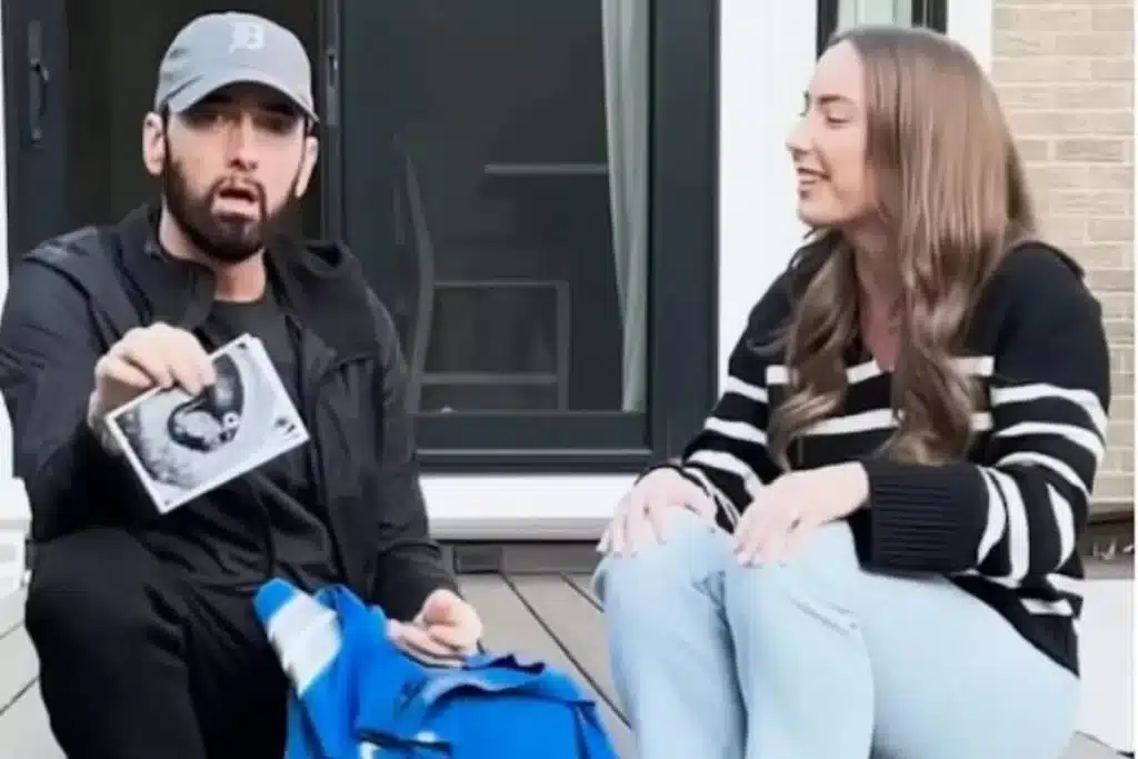 O rapper Eminem com sua filha, Hailie Jade, sentado e segurando uma imagem de ultrassom, enquanto ela sorri ao seu lado.
