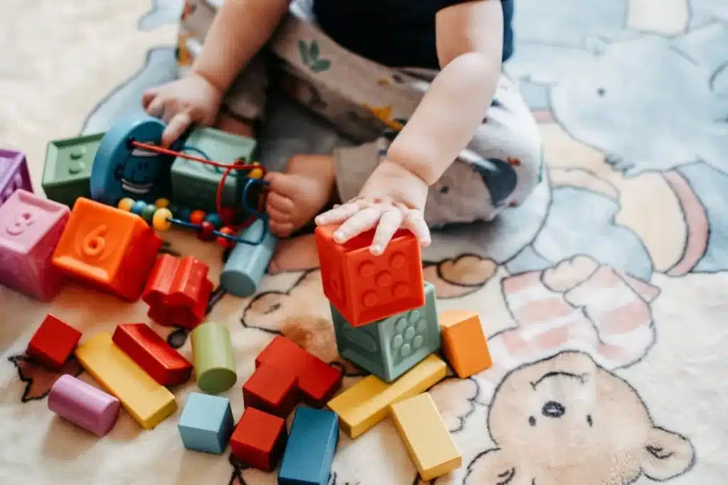 Bebê brincando no chão com diversos blocos coloridos e brinquedos sensoriais, ideais para crianças de 1 ano.