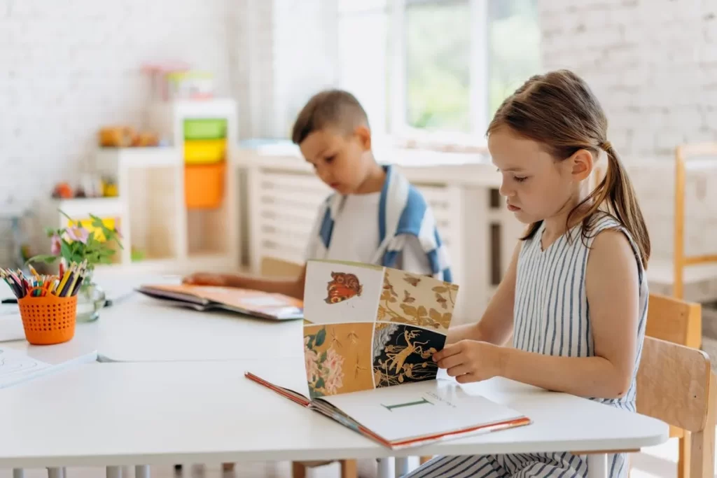 Duas crianças, uma menina e um menino, concentradas lendo livros em um cantinho de leitura claro e convidativo em uma sala de aula no Brasil.