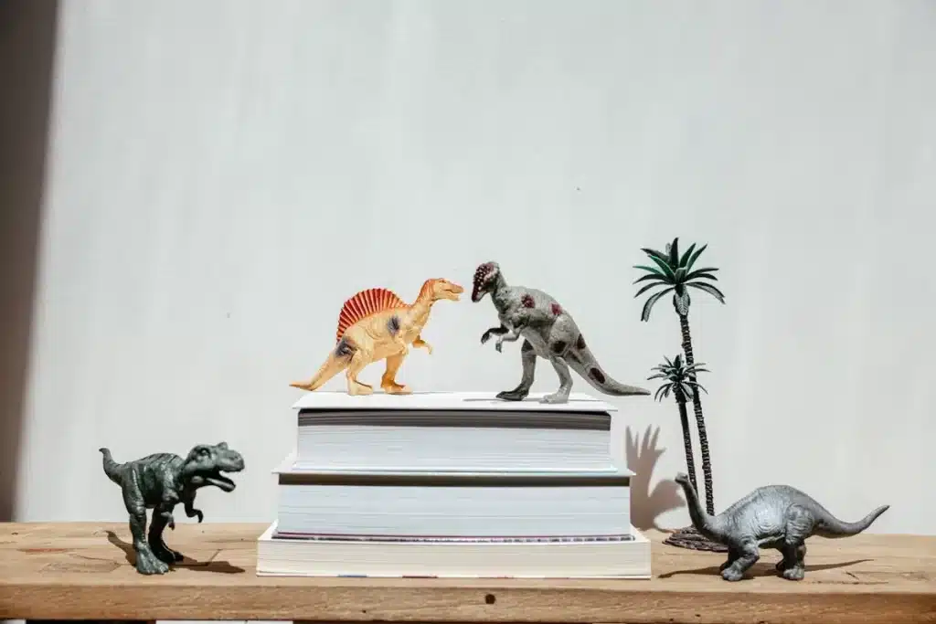  Brinquedos de dinossauros e palmeiras sobre livros, simbolizando escrita criativa, imaginação, fantasia e histórias.