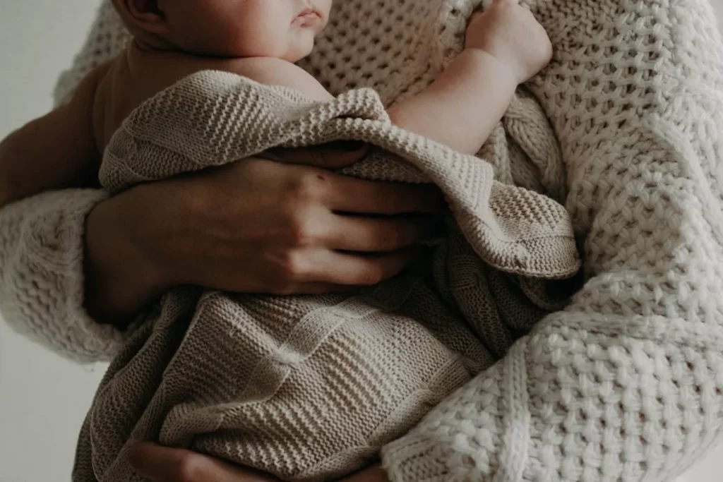 Bebê recém-nascido no colo de sua mãe, envolto em um cobertor de tricô, representando as primeiras fases da infância e o desenvolvimento infantil.  