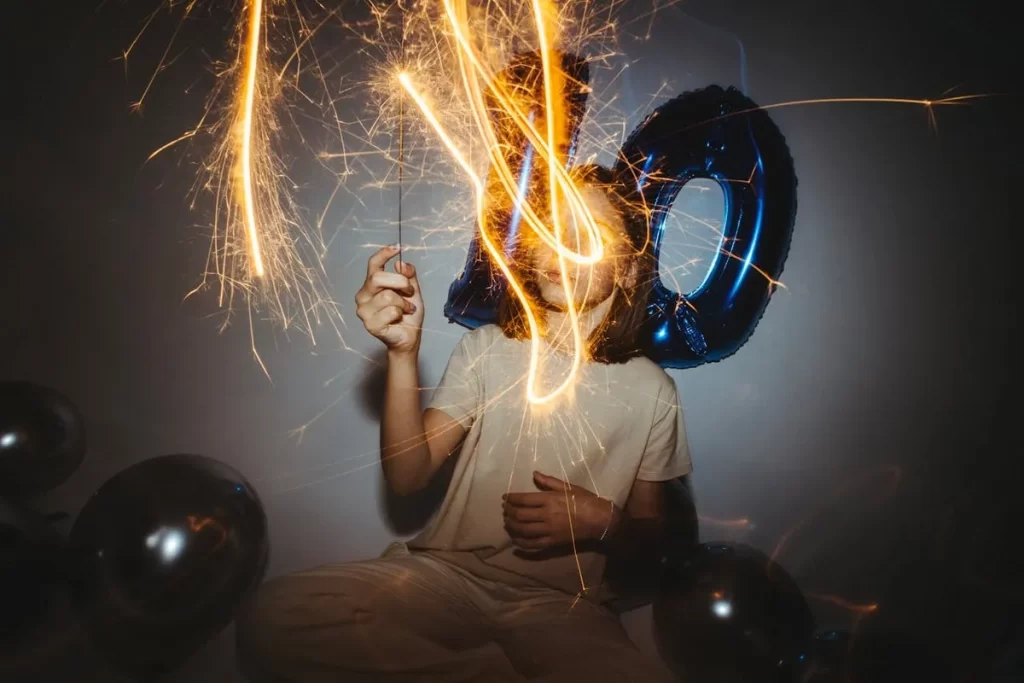 Pessoa sentada com balão de número e sparklers acesos, simbolizando as fases da infância e celebração.