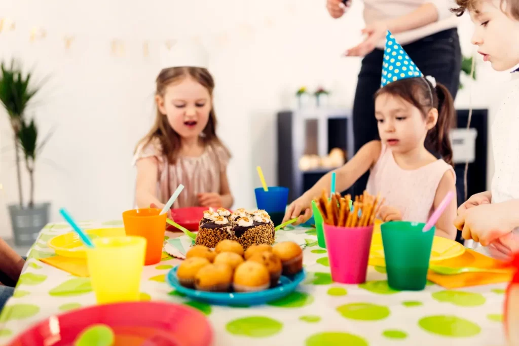 Crianças com chapéus de festa aproveitando bolo, cupcakes e petiscos em festa em casa infantil.