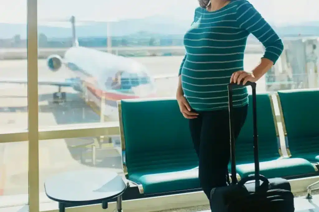 Mulher grávida com mala no aeroporto, observando avião, ilustrando a pergunta "grávida pode viajar de avião" e a segurança da viagem aérea na gestação.
