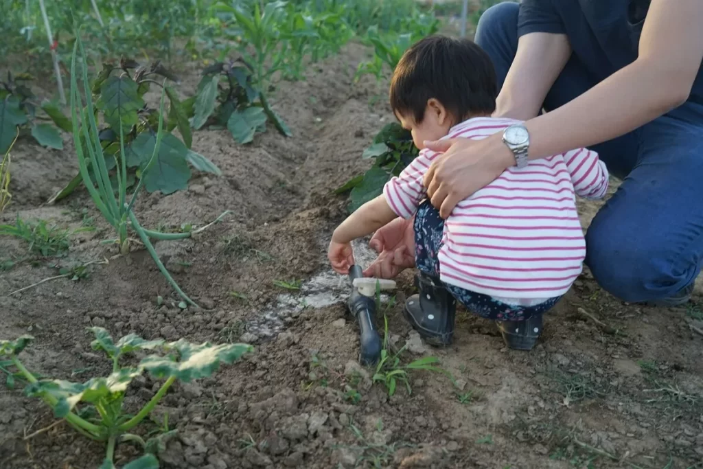Adulto e criança pequena regando plantas em uma horta em casa.
