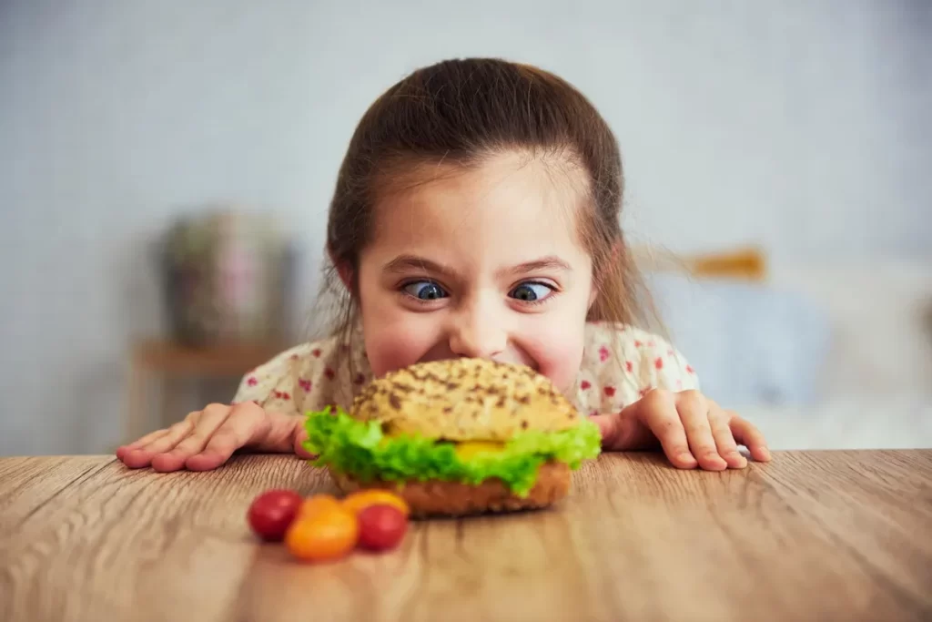 Menina feliz com lanche da tarde saudável, incluindo hambúrguer vegetariano e tomatinhos
