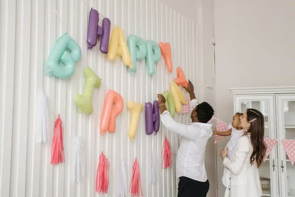Família decorando a parede com balões coloridos que formam a frase "Happy Birthday" para uma festa de aniversário infantil.