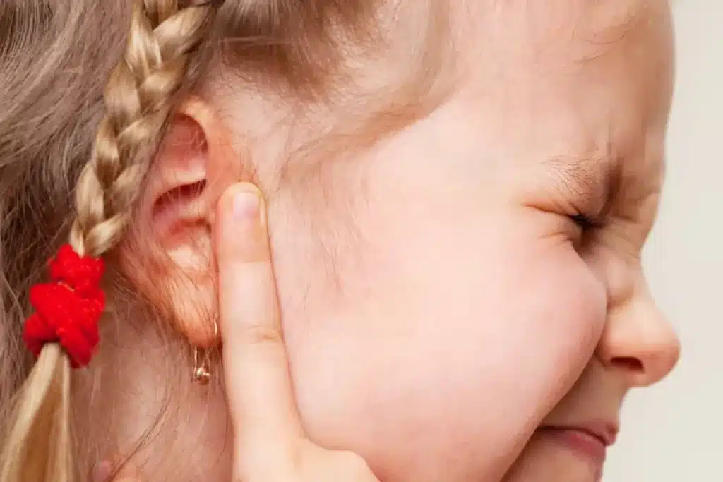  Criança com dor de ouvido, otite média infantil, menina tocando o ouvido com a mão.