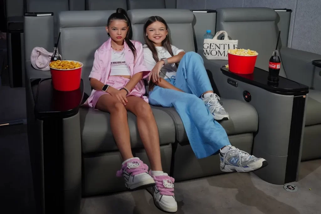 Duas meninas sentadas em poltronas de cinema com baldes de pipoca e bebidas. A imagem representa o período da pré-adolescência, uma fase de transição e crescimento, relevante para a definição de até que idade é criança.