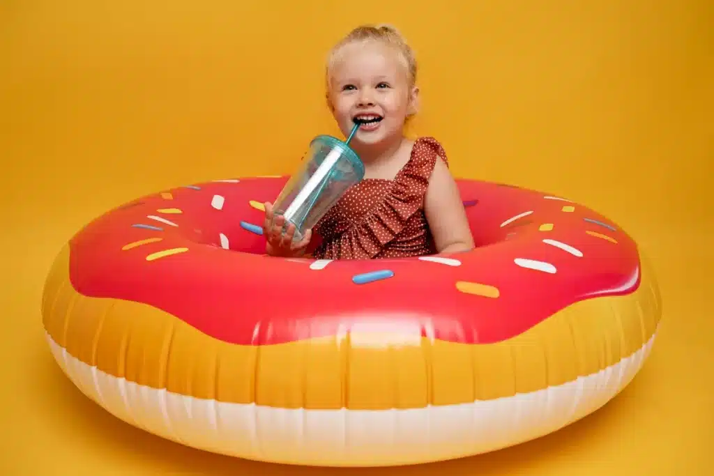 Criança sorridente sentada dentro de uma boia inflável em formato de donut, perfeita para diversão em piscina inflável.