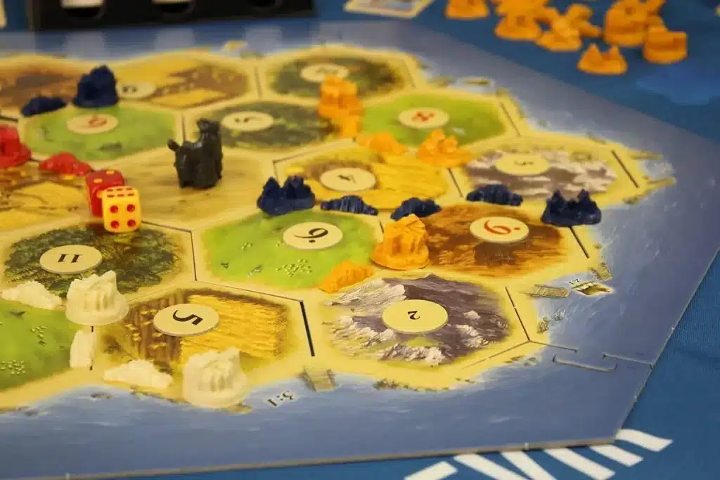 O tabuleiro do jogo de estratégia Catan com peças de madeira, dados e cartas de recursos. A imagem representa o jogo de tabuleiro mais famoso do mundo.