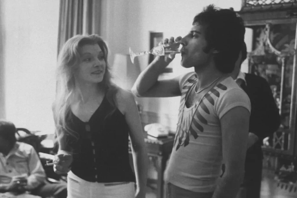 Fotografia em preto e branco de Freddie Mercury bebendo champanhe ao lado de Mary Austin.