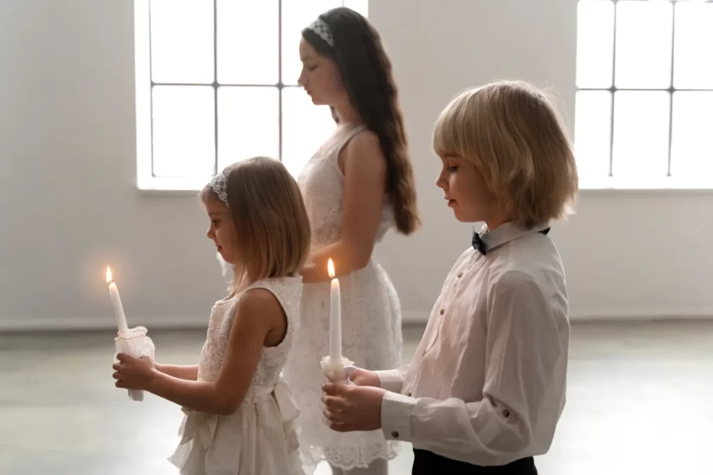 Três crianças com roupas brancas, segurando velas acesas, em uma cerimônia de Primeira Comunhão.
