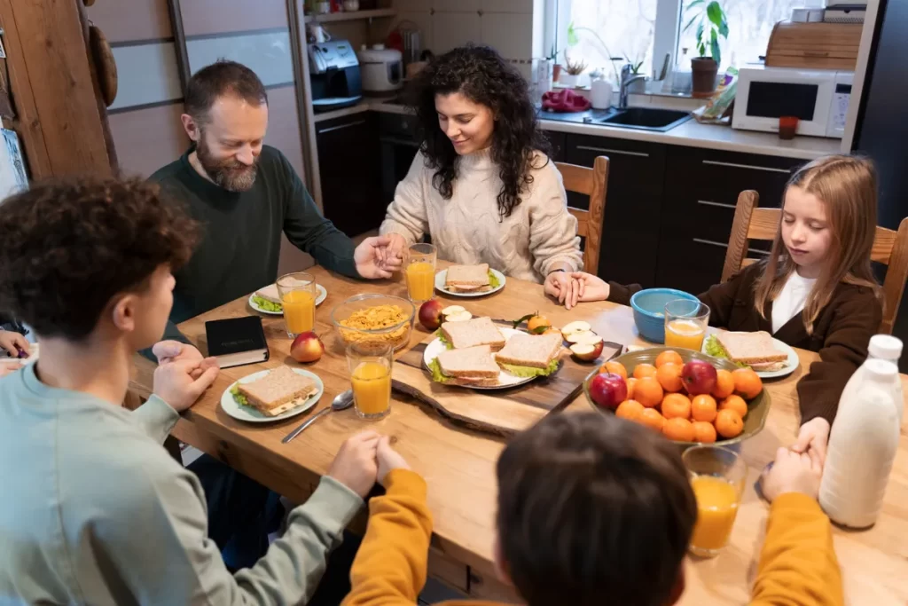 Família fazendo uma oração antes do almoço, com as mãos dadas, mostrando união, gratidão e o amor que os une.