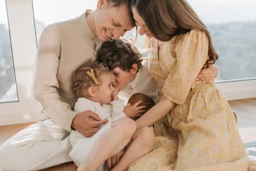 Família demonstrando amor ao próximo, com os pais abraçando carinhosamente seus filhos, em uma cena que transmite afeto e união.