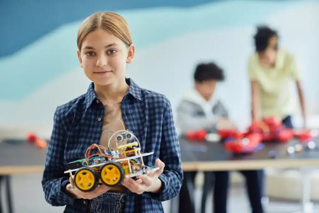 Menina sorrindo e segurando um robô em uma feira de ciências, demonstrando o resultado de seu trabalho e criatividade.