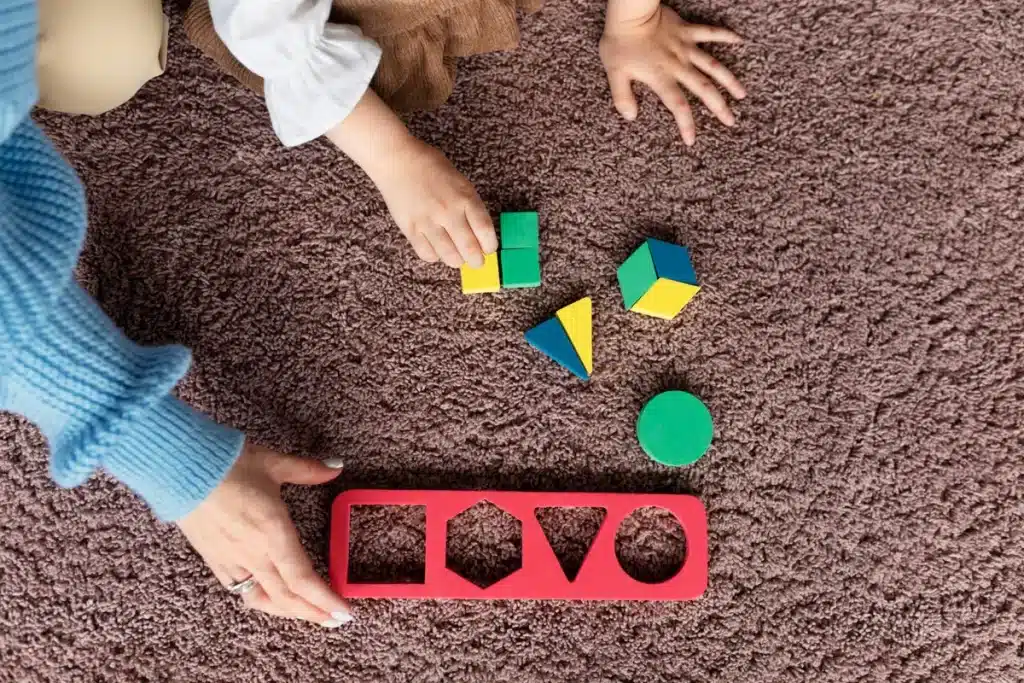 Aprendizagem multissensorial com um adulto e uma criança brincando com formas e cores em um tapete.