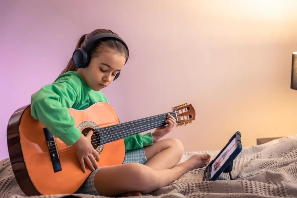 Menina tocando violão e usando fones de ouvido enquanto segue uma aula online, mostrando a beleza e o aprendizado de uma música de louvor.