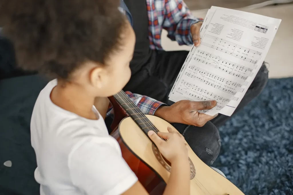 Pai e filha tocando violão e lendo uma partitura, em um momento de aprendizado e conexão através da música de louvor.