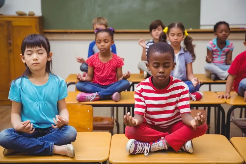 Crianças em sala de aula praticando atenção plena ou meditação em suas carteiras.