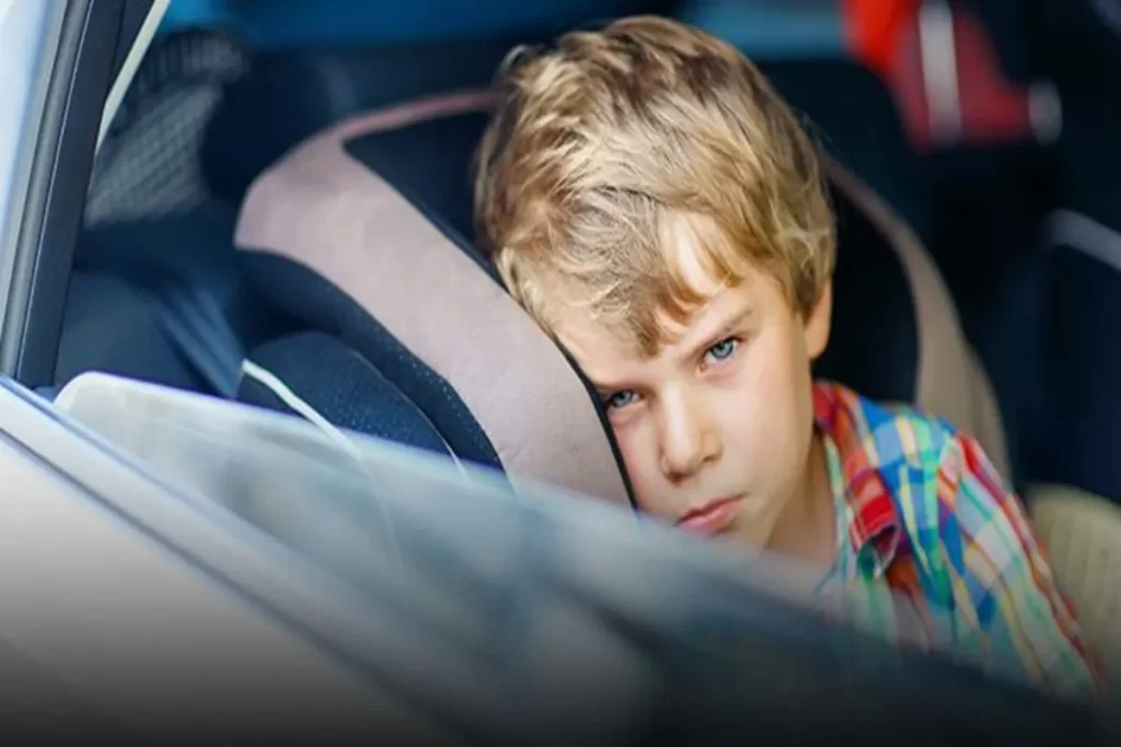 Criança com expressão de enjoo de movimento no carro, apoiada no banco e com um olhar de desconforto.