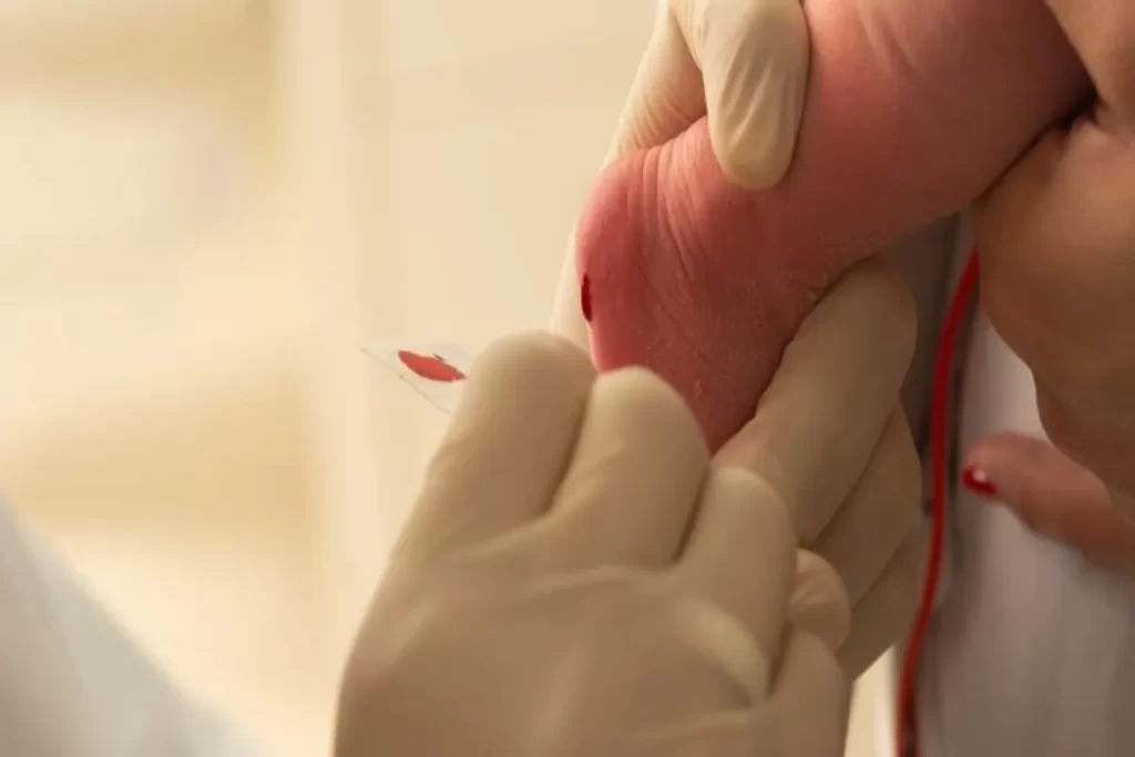 Profissional de saúde, usando luvas, coleta amostra de sangue do calcanhar de um recém-nascido para o exame do pezinho.