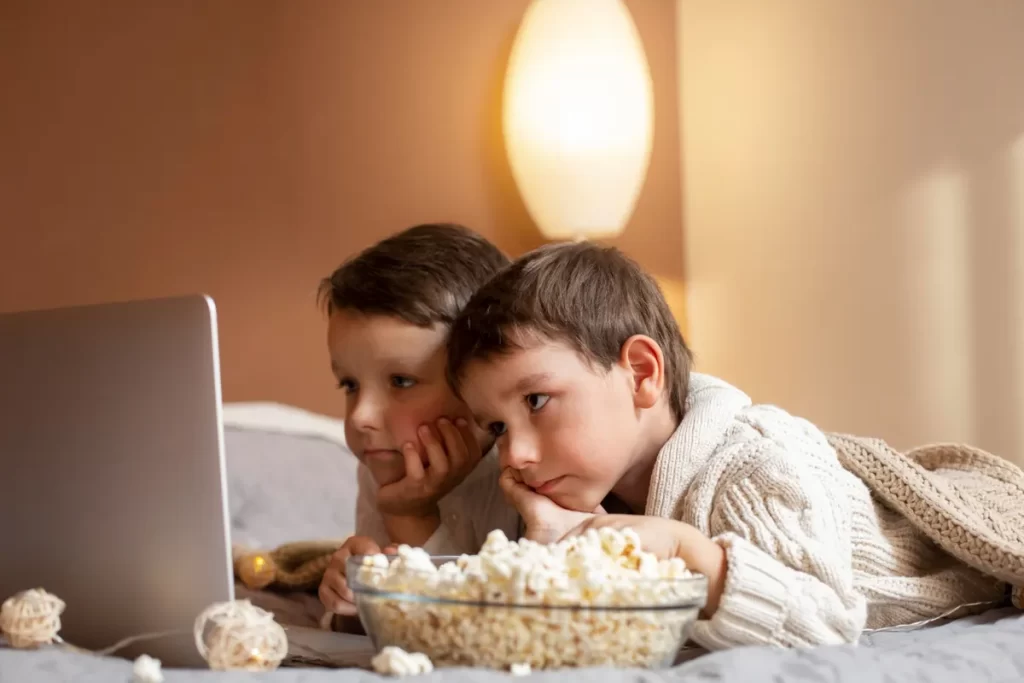 Dois meninos assistindo filme em casa com tigela de pipoca