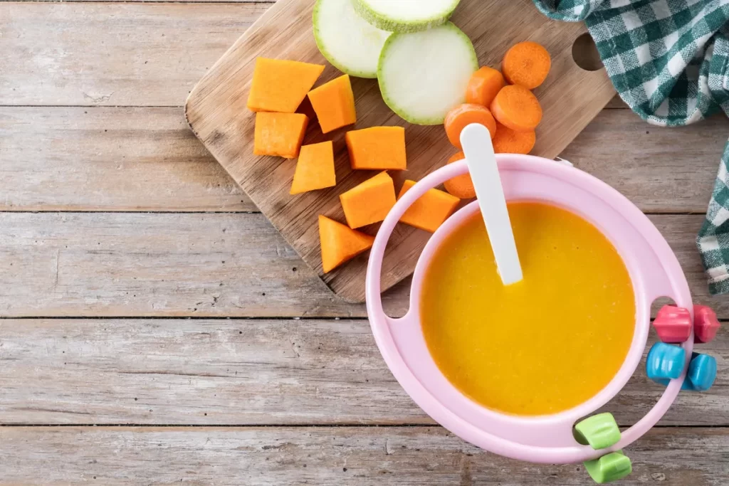Sopinha de legumes simples no prato infantil com cenoura, abóbora e abobrinha.