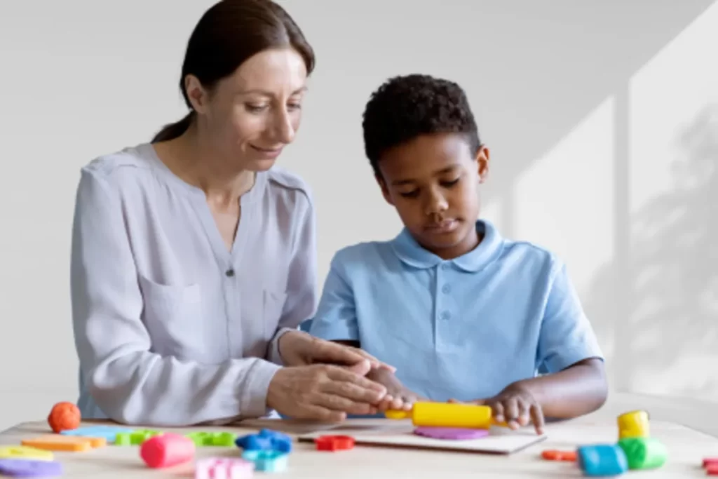 Criança em sessão de terapia ocupacional com terapeuta, utilizando massinha colorida para desenvolver habilidades motoras e cognitivas.